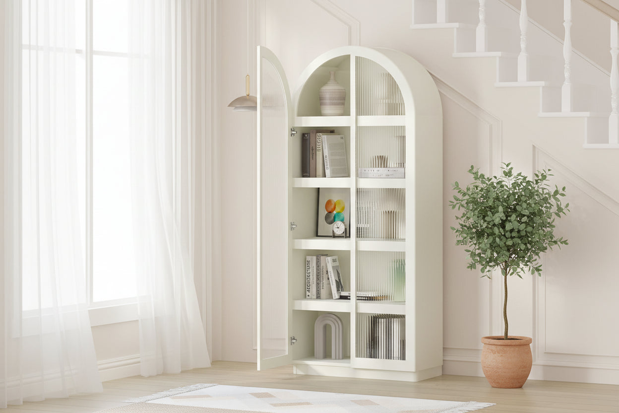 White curved bookshelf with books and decor items in a room with a plant and stool.