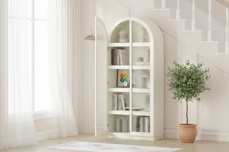 White curved bookshelf with books and decor items in a room with a plant and stool.