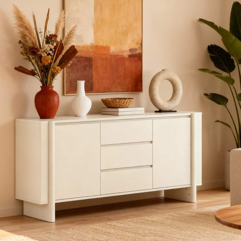 White sideboard with decorative items in a room with a painting and plant.
