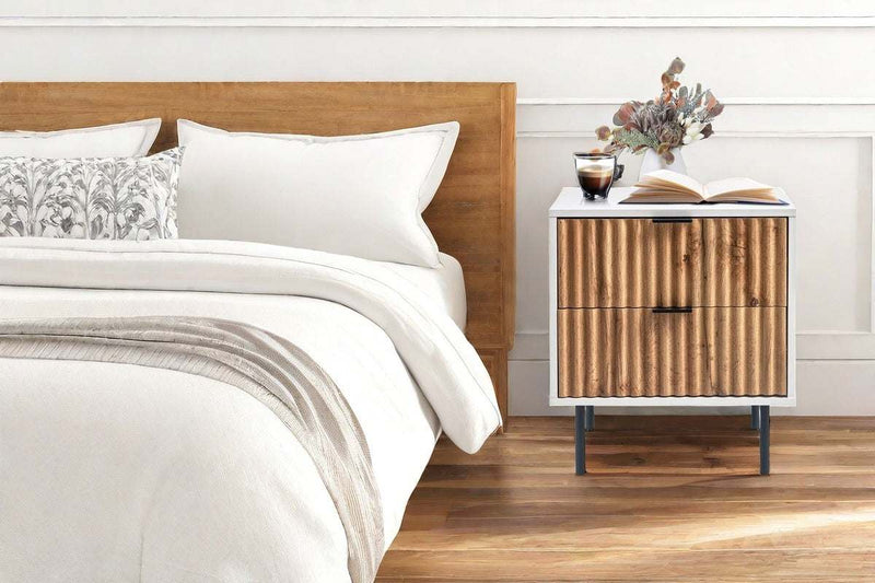 Chelsea 2-Drawer Bedside Table with wavy timber front, sleek black handles, and mid-century metal legs against a stylish bedroom setting.